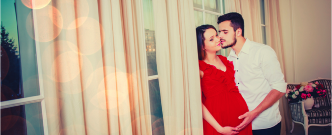 man kissing pregnant wife in front of windows