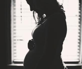 pregnant woman with hands on her belly standing in front of a window