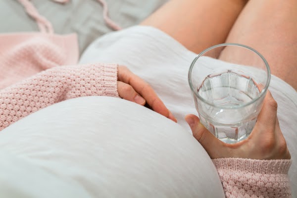 pregnant woman holding glass of water while sitting
