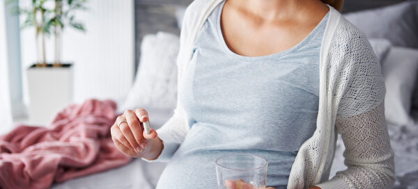 pregnant woman holding vitamins and a glass of water